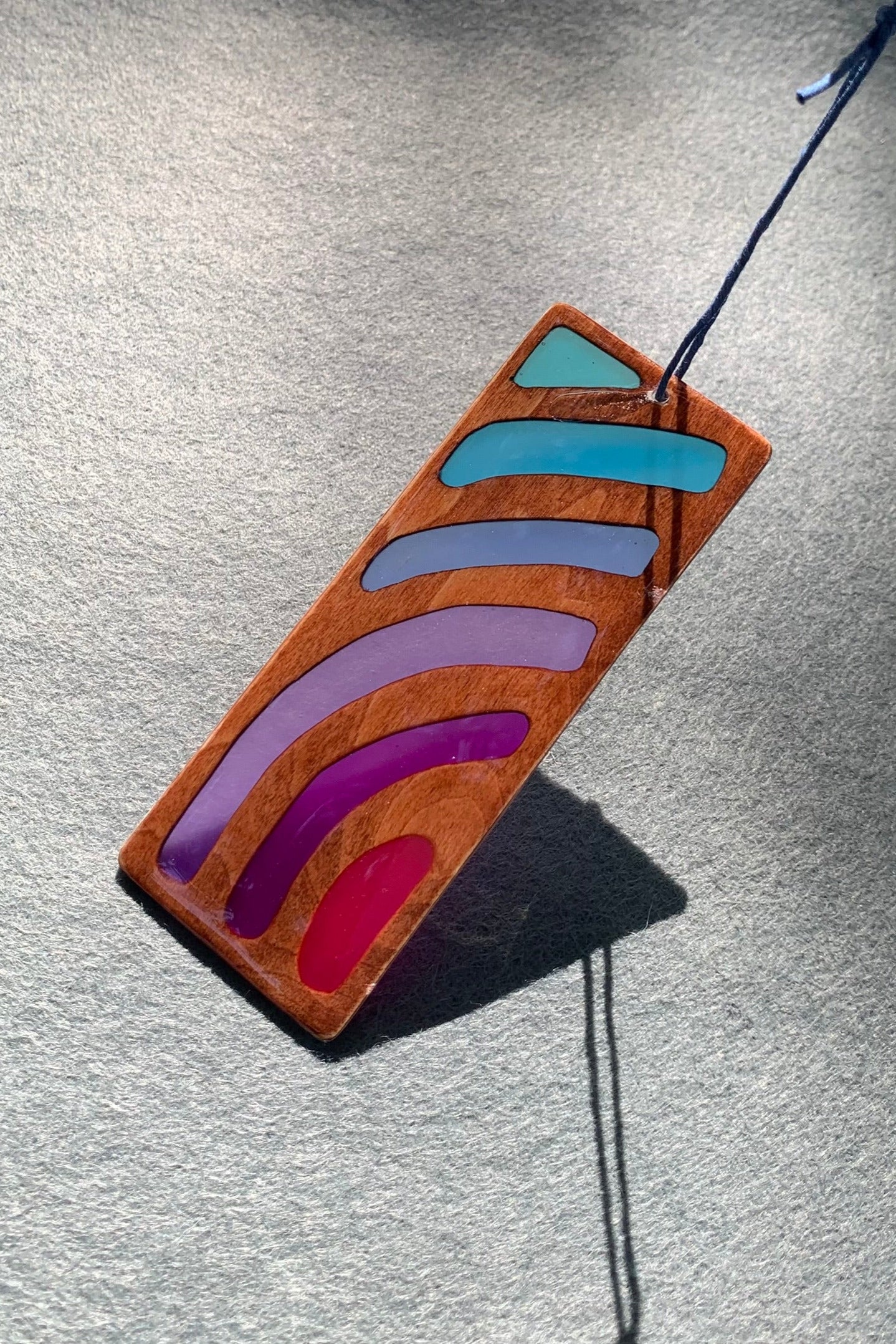 Hand cut wooden bookmark with curved lines emanating an abstract sunset vibe with UV resin translucent colors