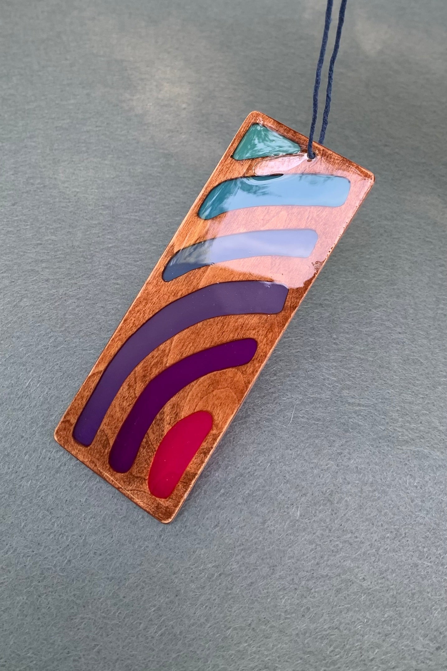 Hand cut wooden bookmark with curved lines emanating an abstract sunset vibe with UV resin translucent colors